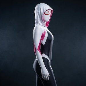 May include: A full-body hooded bodysuit featuring a white hood and sleeves with pink web-patterned accents, contrasted by a black torso with a textured dot pattern. The mask is white with large, outlined red eye lenses covering the face area.