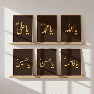 May include: Six framed art prints with gold calligraphy on a dark brown background. The prints are arranged in two rows of three, displayed on wooden shelves against a white wall. The calligraphy features Arabic script.