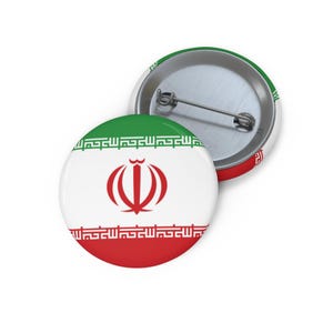 Puede incluir: Dos insignias redondas con la bandera iraní. Las insignias muestran los colores de la bandera: verde, blanco y rojo, con el emblema en el centro. Una insignia está delante y la otra ligeramente detrás.