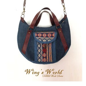 May include: A blue denim handbag with a brown leather strap and handle. The bag has a front pocket with a colorful geometric pattern. The text "Wing's World Dream Work Series" is printed below the bag.