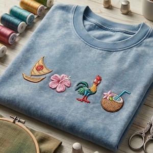 Pode incluir: Uma camisola de gola redonda azul-clara com quatro bordados: um veleiro bege com uma espiral vermelha, uma flor de hibisco cor-de-rosa, um galo colorido com penas vermelhas e azuis e um coco com uma palhinha azul.