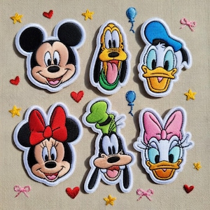Könnte beinhalten: Ein Set aus sechs gestickten Aufnähern mit den Gesichtern von Mickey Maus, Minnie Maus, Pluto, Donald Duck, Goofy und Daisy Duck, angeordnet auf einem strukturierten beigen Hintergrund mit kleinen gestickten roten Herzen, gelben Sternen und blauen Ballons.