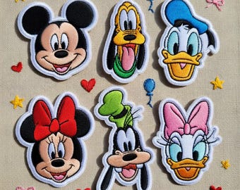 May include: A set of six embroidered patches featuring the faces of Mickey Mouse, Minnie Mouse, Pluto, Donald Duck, Goofy, and Daisy Duck, arranged on a textured beige background with small embroidered red hearts, yellow stars, and blue balloons.
