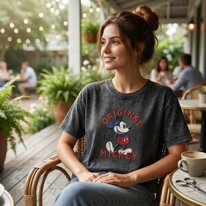 Puede incluir: Una camiseta de manga corta gris carb&oacute;n con un gr&aacute;fico de Mickey Mouse con pantalones cortos rojos y zapatos amarillos, con el texto rojo "ORIGINAL" arriba, "19 28" en el medio y "MICKEY" abajo, combinada con pantalones vaqueros azules.