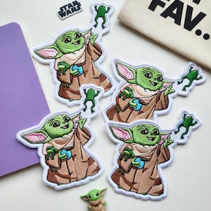 May include: Four embroidered patches featuring a green character with large ears wearing a tan robe, holding a blue sphere and small green frogs. A small Star Wars logo patch and a miniature figurine of the same character are also included.