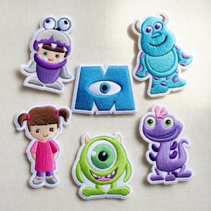 May include: A set of six embroidered patches featuring a purple monster in a grey costume, a blue furry monster with purple spots, a blue letter M with a central eye, a girl with brown pigtails in a pink dress, a green one-eyed monster, and a purple lizard.