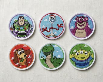 May include: Six circular embroidered patches featuring characters from the animated film series. Characters include Buzz Lightyear, Forky, Lotso, Slinky Dog, Rex, and an Alien. Each patch has a white border and a light blue sky background.