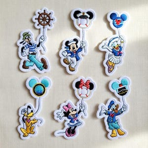 May include: Embroidered patches of Disney characters in sailor outfits. Mickey, Minnie, Donald, Daisy, Goofy, and Pluto are depicted. Each patch is white-outlined and holds a nautical-themed item, such as a ship's wheel or life ring.