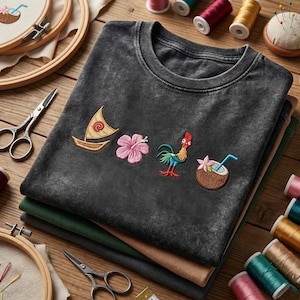 Pode incluir: Uma t-shirt cinzenta-carv&atilde;o com efeito de lavagem &aacute;cida, apresentando quatro &iacute;cones bordados: um veleiro bege com uma espiral vermelha, uma flor de hibisco rosa, um galo colorido e um coco castanho com uma flor rosa e uma palhinha azul.