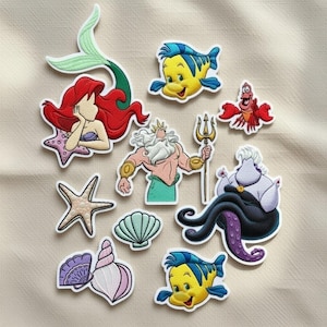 Op de afbeelding: Een verzameling geborduurde patches met personages uit een populaire animatiefilm. Bevat Ariel met rood haar, Botje, Koning Triton, Sebastiaan, Ursula en andere ontwerpen met zeethema. De patches hebben een witte rand.