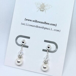 May include: A pair of silver dangle earrings with a small crystal bead and a white pearl drop. The earrings are displayed on a white card with the website address {www.willowandbee.com} and email address {willowandbee@gmail.com}.