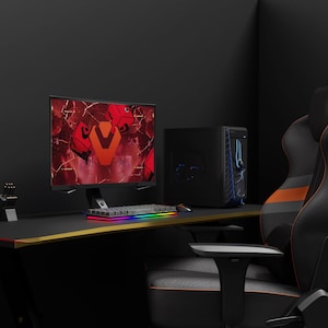 May include: A black gaming desk with a black and orange gaming chair. The desk has a black monitor with a red and orange graphic on the screen, a black keyboard with rainbow lighting, and a black computer tower.