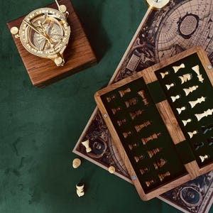 Op de afbeelding: Een houten schaakset met een groene viltinleg en een kompas op een houten doos. De schaakstukken zijn op het bord gerangschikt en het kompas bevindt zich in het midden van de doos. De schaakset staat op een groene ondergrond en het kompas op een bruine ondergrond.