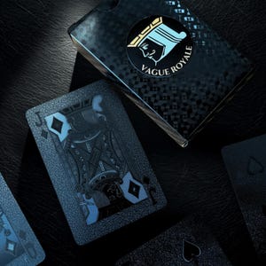 Puede incluir: Un juego de cartas con un esquema de color negro y azul. Las cartas presentan un diseño detallado con un símbolo de diamantes y la letra "J". La caja de cartas tiene las palabras "Vague Royale" y un gráfico de una reina.