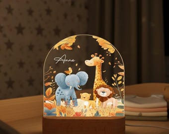 May include: A decorative night light featuring a jungle scene with an elephant, giraffe, lion, and other animals. The light has a wooden base and a clear, arched top with the name "Anna" in script.