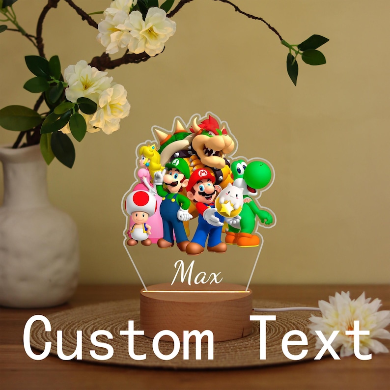 May include: A custom-made night light featuring a group of colorful cartoon characters, including Mario, Luigi, and Yoshi. The light has a wooden base and the name "Max" is printed on the front. The words "Custom Text" are also visible.