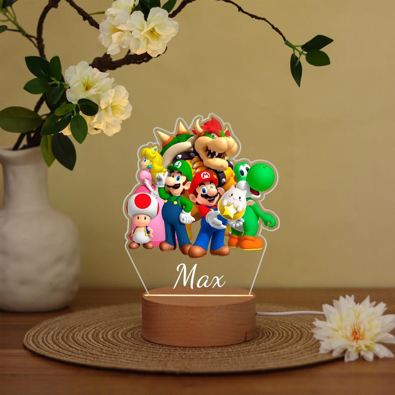 May include: A decorative night light featuring a group of colorful cartoon characters, including Mario, Luigi, and Yoshi. The characters are on a clear acrylic panel, with the name "Max" below. The base is made of wood.