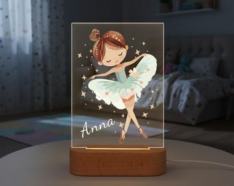 Może przedstawiać: Prostokątna lampka nocna z drewnianą podstawą, przedstawiająca baletnicę z kreskówki w jasnoniebieskim tutu. Imię baletnicy, "Anna", jest napisane kursywą. Tło ma akcenty gwiazd.