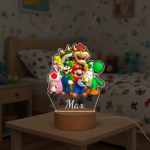 May include: A night light featuring a group of colorful cartoon characters, including Mario, Luigi, and Yoshi. The characters are arranged on a clear acrylic panel, with the name "Max" printed below. The base is made of wood.