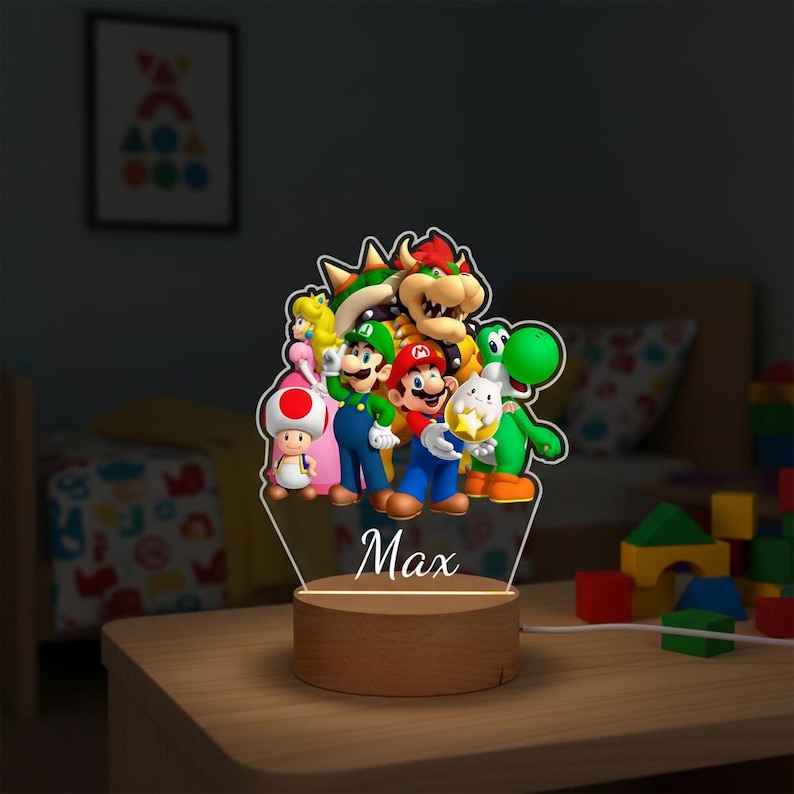 May include: A decorative night light featuring a group of colorful Super Mario characters. The light has a wooden base and a clear acrylic panel with the name "Max" printed on it. The characters include Mario, Luigi, Yoshi, and others.