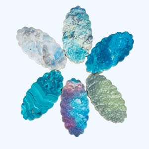 May include: Six oval-shaped decorative pieces with scalloped edges arranged in a circular pattern. Each piece features a distinct surface texture and color, including shades of blue, white, green, and purple, resembling various mineral patterns.