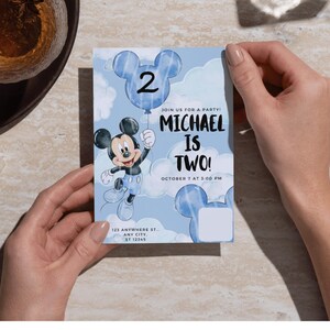 May include: A rectangular birthday invitation card featuring a light blue sky background with white clouds. It displays a cartoon mouse character holding a blue balloon with the number 2. Text reads: JOIN US FOR A PARTY! MICHAEL IS TWO! OCTOBER 7 AT 3:00 PM, 123 ANYWHERE ST., ANY CITY, ST 12345.