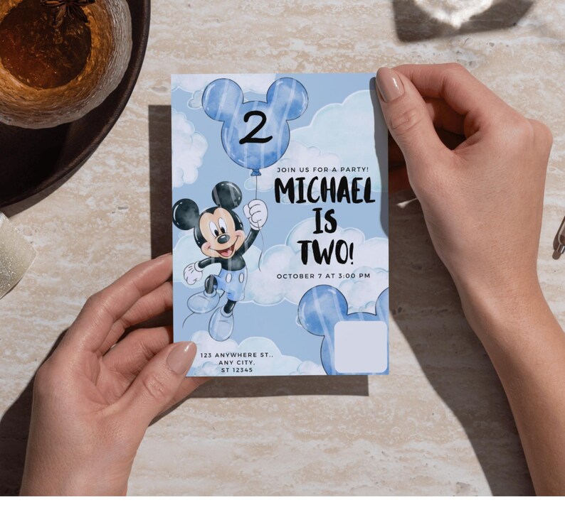 May include: A rectangular birthday invitation card featuring a light blue sky background with white clouds. It displays a cartoon mouse character holding a blue balloon with the number 2. Text reads: JOIN US FOR A PARTY! MICHAEL IS TWO! OCTOBER 7 AT 3:00 PM, 123 ANYWHERE ST., ANY CITY, ST 12345.