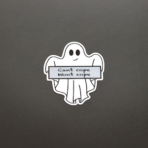 Peut inclure: Autocollant blanc en forme de fantôme souriant, tenant une pancarte grise avec le texte "Can't cope, Won't cope". L'autocollant est sur un fond gris foncé. Le design est simple et de style dessin animé.