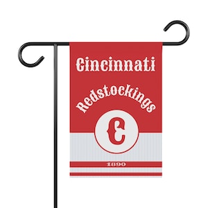 Könnte beinhalten: Eine rot-weiße Cincinnati Redstockings Gartenflagge. Die Flagge zeigt den Namen und das Logo des Teams mit dem Jahr 1890 am unteren Rand. Sie ist auf einem schwarzen Metallständer montiert.