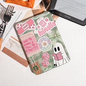 Könnte beinhalten: Eine grün-weiß karierte Kindle-Hülle mit Aufklebern. Die Aufkleber enthalten den Text "In My Kindle Era", "Pretty Girls Read Books" und einen Geist, der ein Buch liest. Weitere Aufkleber sind ein Starbucks-Becher und Würfel.
