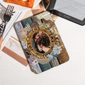 Könnte beinhalten: Eine dekorative Handyhülle im Buch-Design mit einem goldgerahmten Bild eines Paares, Schmetterlingen und floralen Akzenten. Die Hülle enthält Buchtitel wie "Pride and Prejudice" und "Emma". Im Hintergrund ist ein Kindle-E-Reader zu sehen.