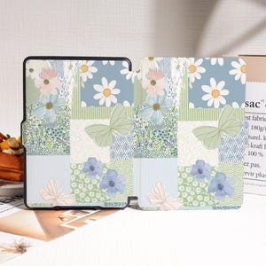 May include: A floral patterned tablet case with a patchwork design. The case features daisies, butterflies, and blue and pink flowers on a light blue, green, and white background. The case is open, revealing the interior.
