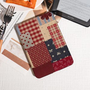 May include: A patchwork Kindle cover with a mix of patterns, including red hearts, plaid, and floral designs. The cover features red, cream, and navy blue fabrics. The word "kindle" is visible on the device.
