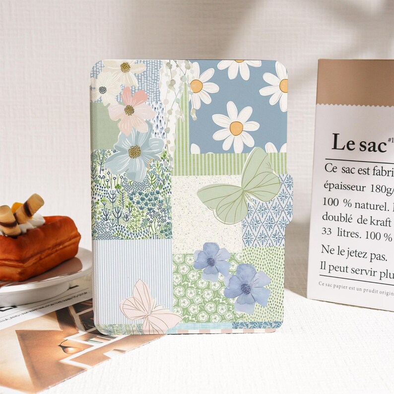 May include: A floral patterned notebook with a patchwork design. The cover features daisies, butterflies, and blue and green floral patterns. The notebook has a rectangular shape and is likely for writing or sketching.