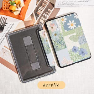 May include: A clear acrylic tablet case with a gray stand and a floral patterned cover. The cover features a patchwork design with daisies, butterflies, and other flowers in shades of blue, green, and pink. The word "acrylic" is printed on the bottom.