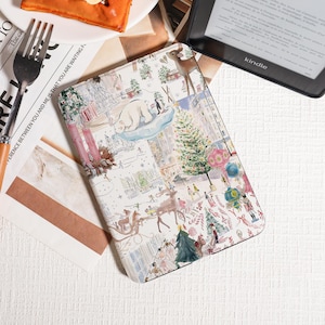 Może przedstawiać: Białe etui na Kindle z fantazyjną zimową sceną. Przedstawia niedźwiedzia polarnego na lodowcu, choinkę i postacie w zaśnieżonym krajobrazie. Etui ma kolorową, szczegółową ilustrację.