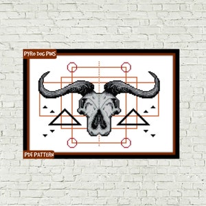 May include: Cross stitch pattern featuring a geometric design with a buffalo skull in the centre. The pattern includes a square frame with circles and triangles in orange and black.