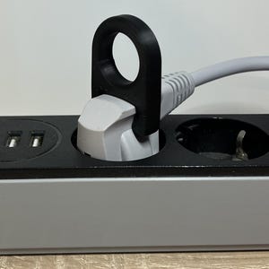May include: A black plastic cord organiser with a loop for easy pulling. The organiser is attached to a white electrical cord plugged into a power strip.