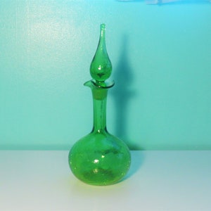 May include: A green glass decanter with a textured surface and a tall, pointed stopper. The decanter has a round body and a long, thin neck.