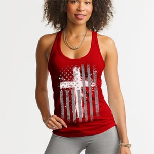 Puede incluir: Una camiseta sin mangas roja con un diseño de bandera estadounidense desgastada y una cruz blanca superpuesta. El diseño de la bandera incorpora estrellas y rayas, creando un tema patriótico y religioso. La camiseta es sin mangas y tiene un estilo de espalda deportiva.