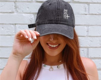 May include: A dark gray baseball cap with the text "JESUS IS KING" in white. The cap has a curved brim and an adjustable strap. The cap is made of a soft, worn material.