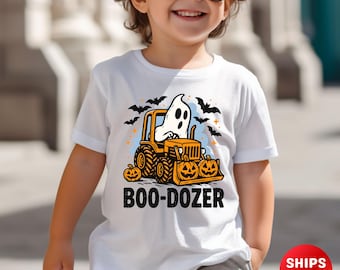 Peut inclure: T-shirt blanc avec un motif sur le thème d'Halloween. Le motif représente un fantôme conduisant un bulldozer jaune avec des seaux de citrouilles, des chauves-souris et le texte "BOO-DOZER".