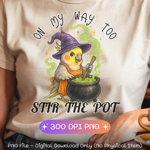 Könnte beinhalten: Beiges T-Shirt mit einem Cartoon-Kakadu, der einen lila Hexenhut und eine orangefarbene Schürze trägt und einen grünen Trank in einem schwarzen Kessel umrührt. Der Text "ON MY WAY TOO" und "STIR THE POT" befinden sich über und unter dem Bild.