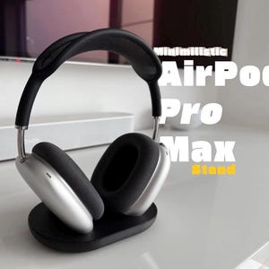 May include: Silver over-ear headphones with black ear cushions and a black headband resting on a black oval-shaped stand. The text "Minimilistic AirPod Pro Max Stand" is visible in white and yellow lettering to the right of the headphones.