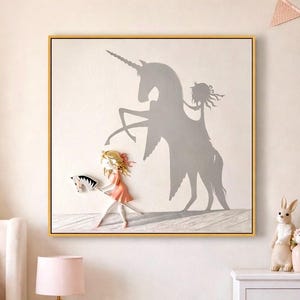 Könnte beinhalten: Ein gerahmtes Kunstwerk zeigt ein Mädchen mit einem Spielzeugpferd, das einen Einhornschatten wirft. Das Kunstwerk befindet sich in einem goldenen Rahmen und hängt in einem rosa Schlafzimmer. Das Mädchen trägt ein rosa Kleid und hat blondes Haar.
