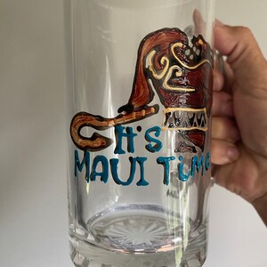 Puede incluir: Una taza de vidrio transparente con un dise&ntilde;o pintado a mano de Maui de la pel&iacute;cula de Disney Moana. El dise&ntilde;o incluye el anzuelo de pesca de Maui y el texto "It's Maui Time".