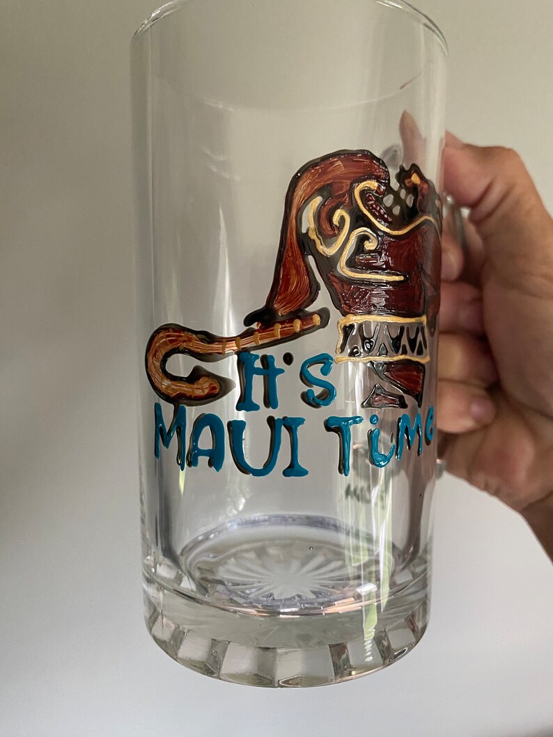 Puede incluir: Una taza de vidrio transparente con un dise&ntilde;o pintado a mano de Maui de la pel&iacute;cula de Disney Moana. El dise&ntilde;o incluye el anzuelo de pesca de Maui y el texto "It's Maui Time".
