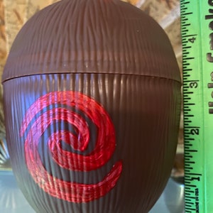 May include: Brown coconut-shaped cup with a red swirl design. The cup is about 6 inches tall and has a straw.
