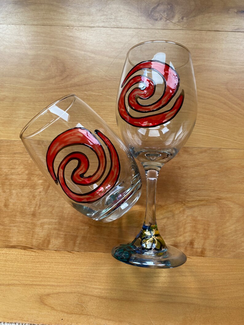 Puede incluir: Dos copas de vino con un dise&ntilde;o de espiral rojo y negro. La copa de la izquierda es un vaso y la copa de la derecha es una copa de vino con tallo.