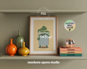 Op de afbeelding: Een ingelijste kunstdruk met een botanische illustratie, tentoongesteld op een plank met decoratieve vazen en boeken. De print toont een plant in een gestreepte pot. De plank bevat ook een discobal en boeken met de titels "Dopamine", "Oxytocine" en "Serotonine".
